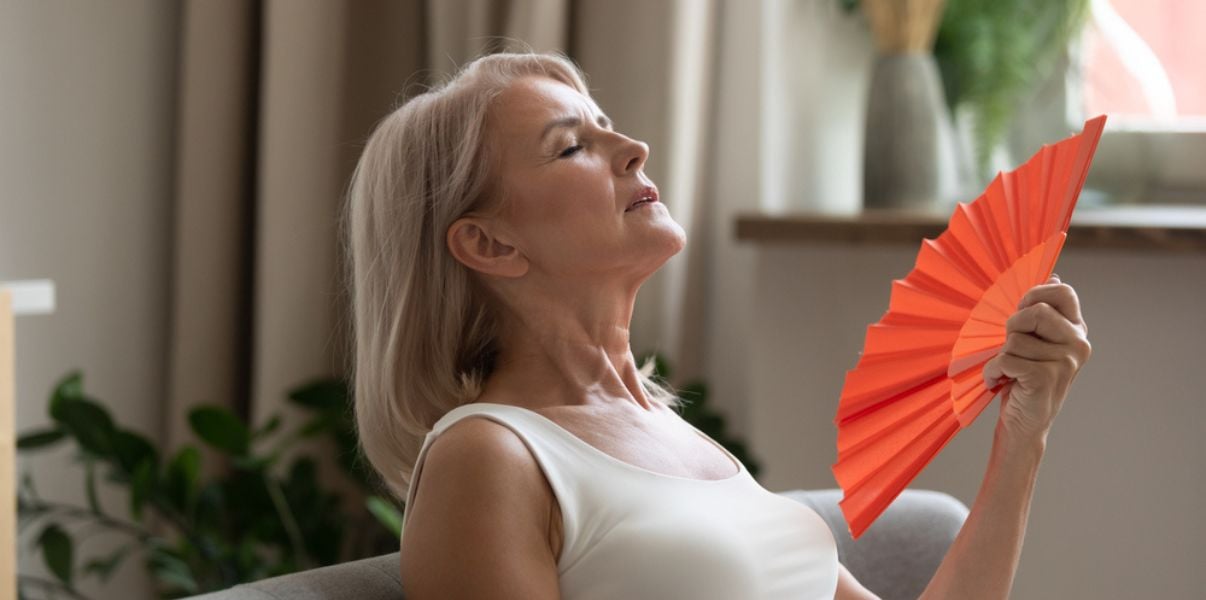 Woman fanning herself and considering transforming her conservatory into an insulated conservatory to stop it from being so hot
