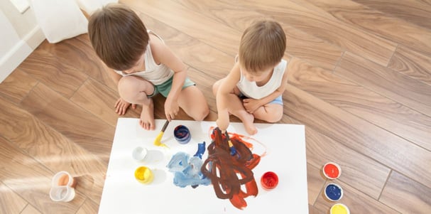 Entertained young sibligns painting together on the floor in their homes insulated conservatory