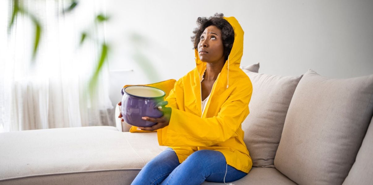 Concerned and annoyed woman sitting on her sofa watching her leaking conservatory roof with a pan  on her lap