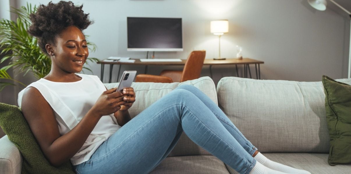 Young female homeowner smiling and using her phone on her sofa, after her leaking conservatory roof was replaced by Projects4Roofing