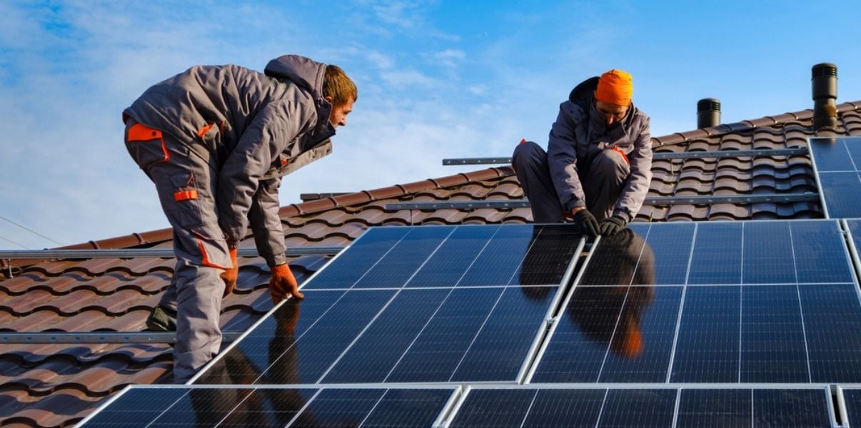 Two men installing solar panels on a houses roof