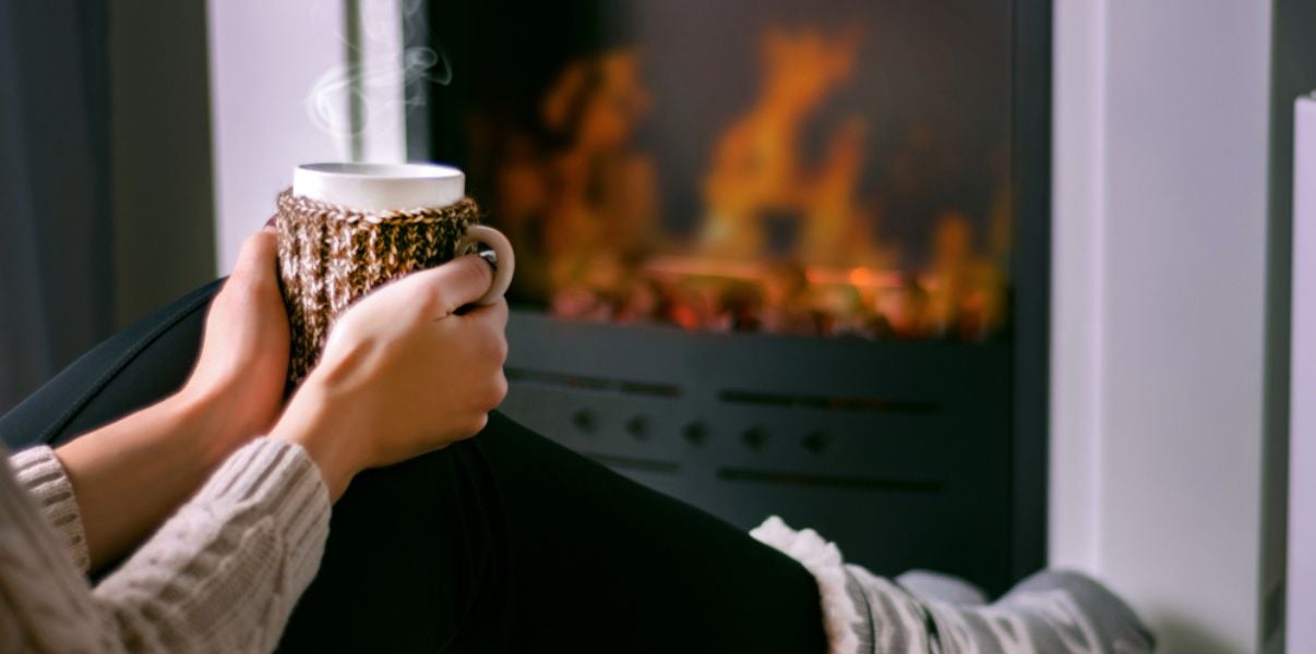 Woman sitting near the fireplace with a warm cup of tea in her hands