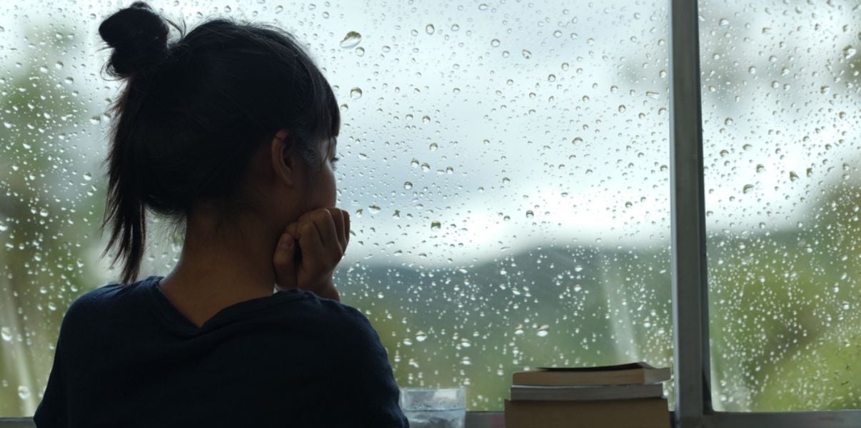 Young girl looking out the windown at a rainy day, thinking about how it will affect her familys conservatory roof replacement project