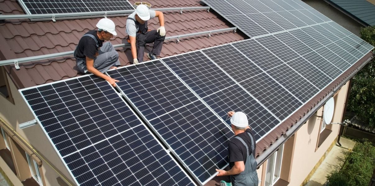 Group of three men installing black solar panels on a houses roof