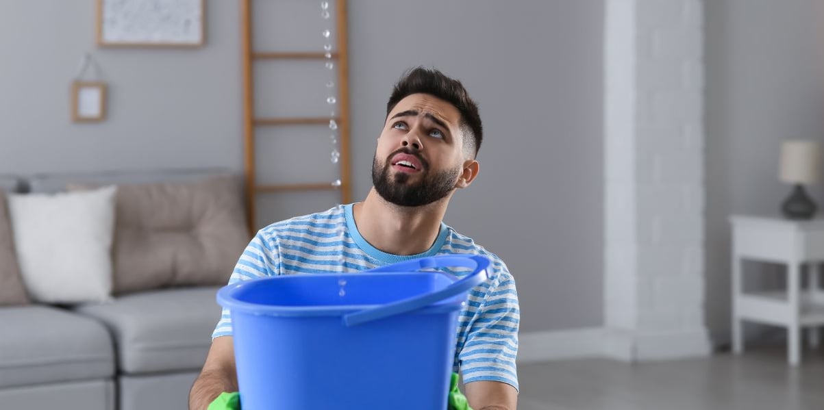 Concerned guy catching water in a bucket due to conservatory roof replaced wrongly