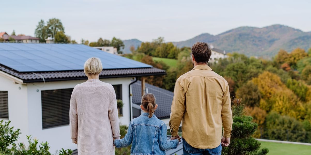 Father, mother, and daughter happily observing the solar panel installation over their homes roof